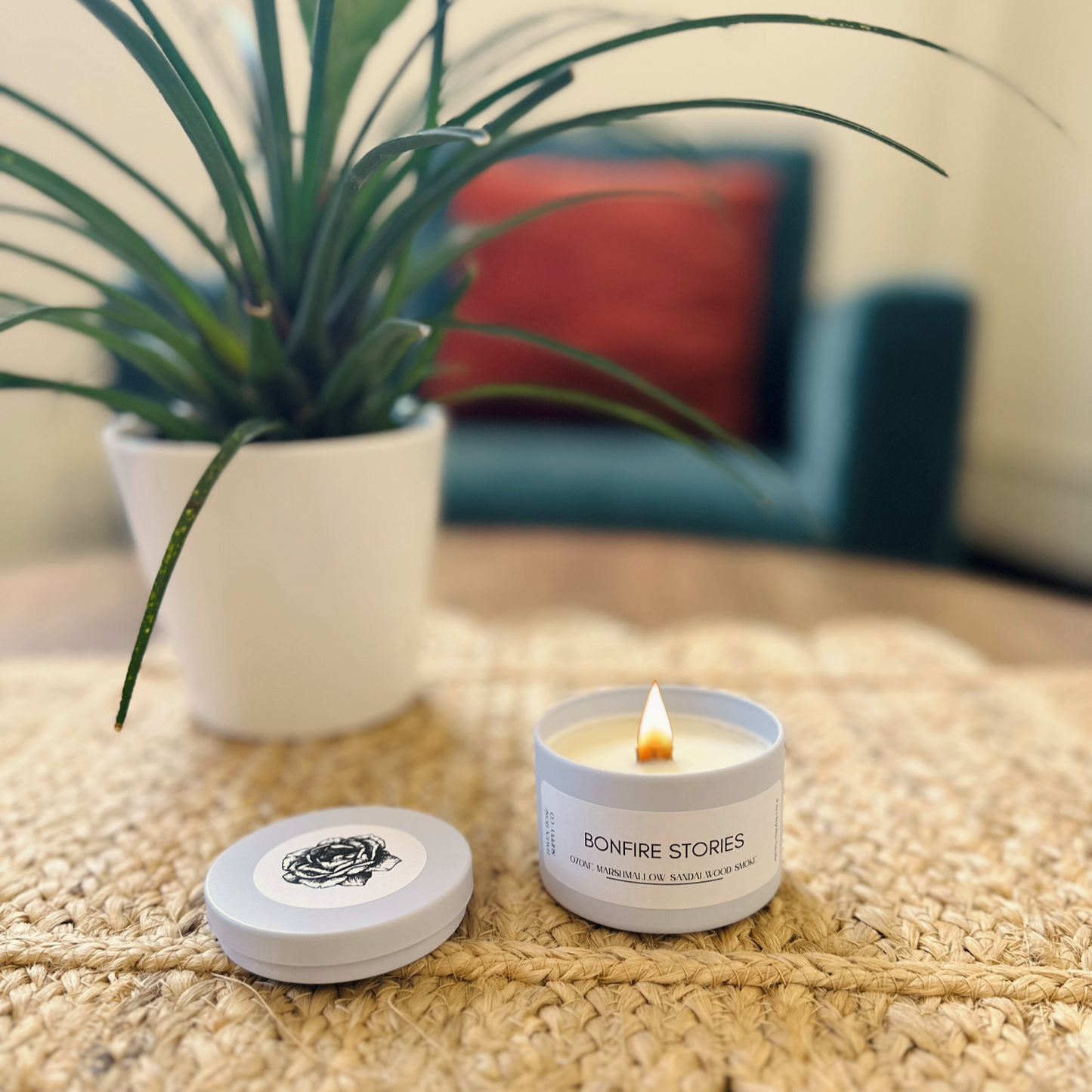Candle with packaging on a textured surface with a plant and cushion in the background